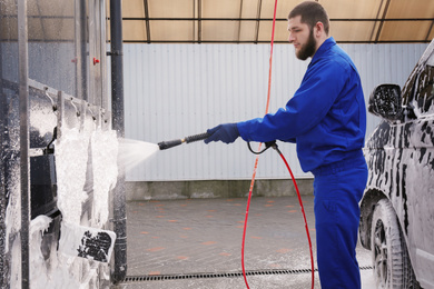 Photo of Worker cleaning automobile floor mats with high pressure water jet at car wash