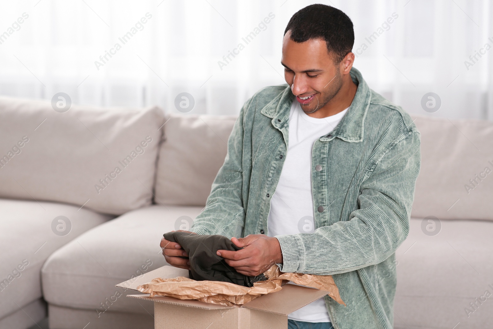 Photo of Happy young man opening parcel at home. Internet shopping