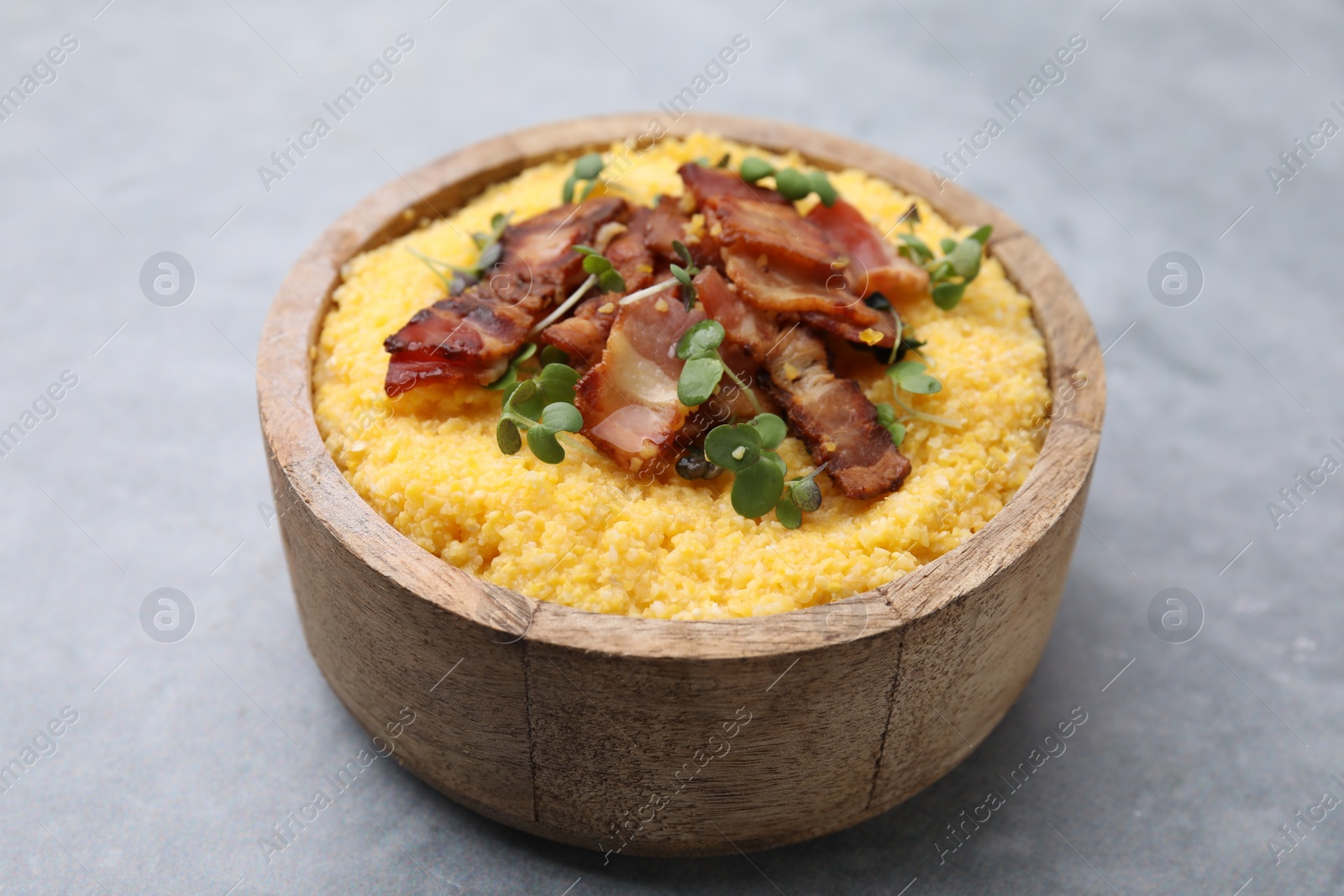 Photo of Cooked cornmeal with bacon and microgreens in bowl on light grey table, closeup