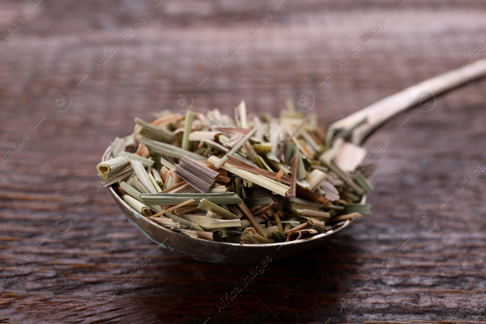 Photo of Metal spoon with aromatic dried lemongrass on wooden table, closeup