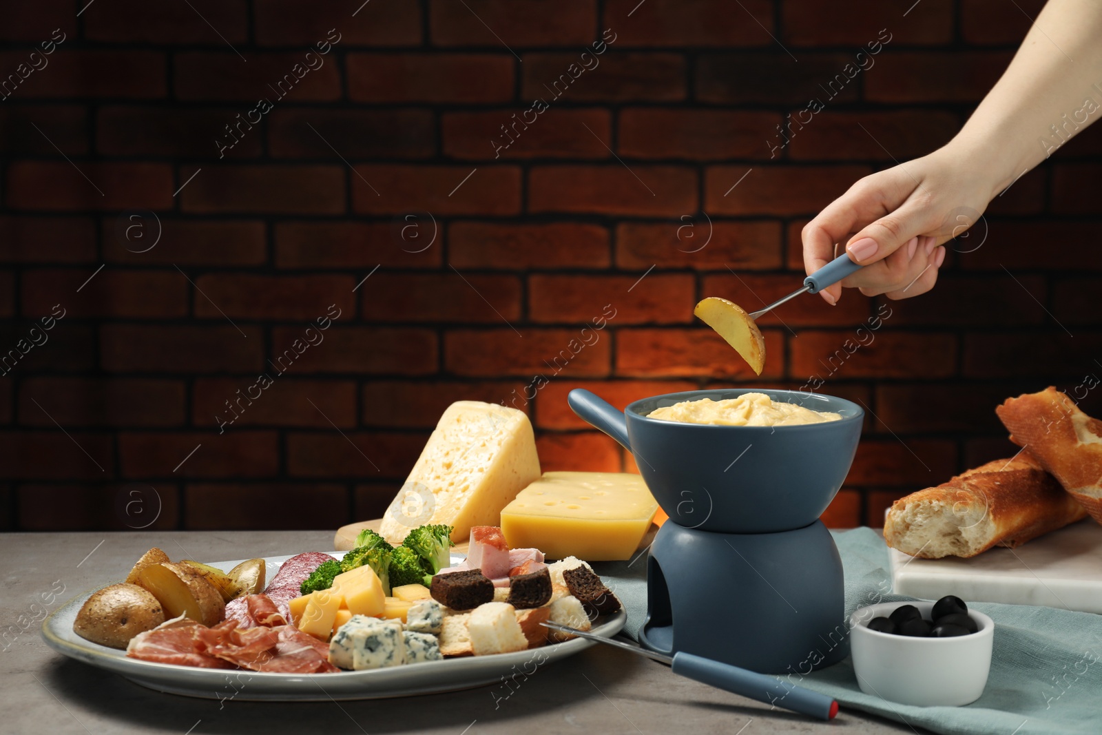 Photo of Woman dipping piece of potato into fondue pot with melted cheese at table with snacks, closeup. Space for text