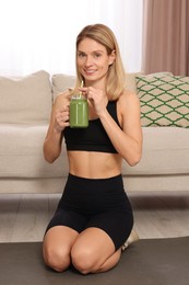 Photo of Young woman in sportswear with mason jar of fresh smoothie at home