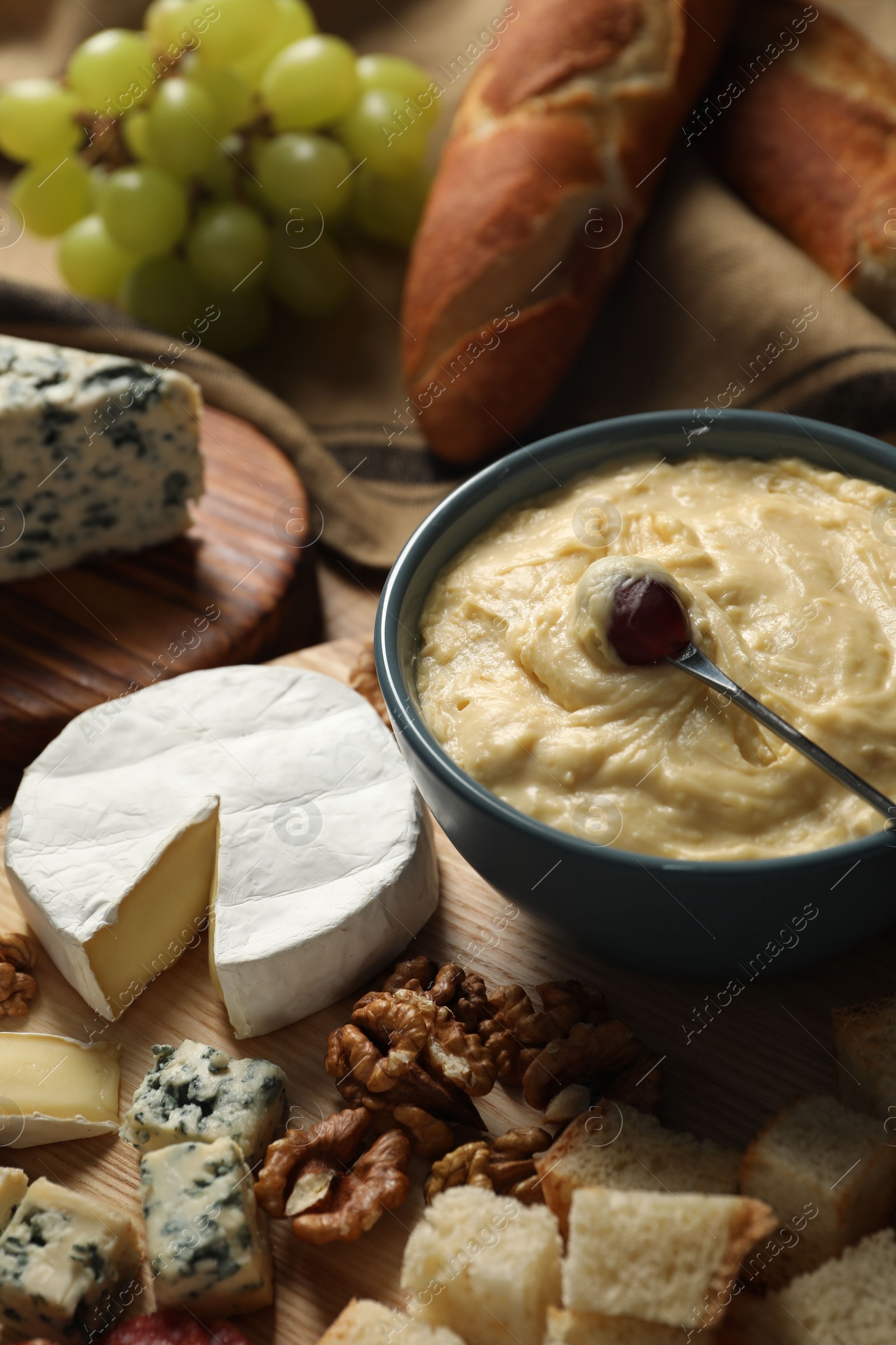 Photo of Fondue pot with tasty melted cheese, fork and different snacks on wooden table