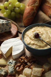 Photo of Fondue pot with tasty melted cheese, fork and different snacks on wooden table