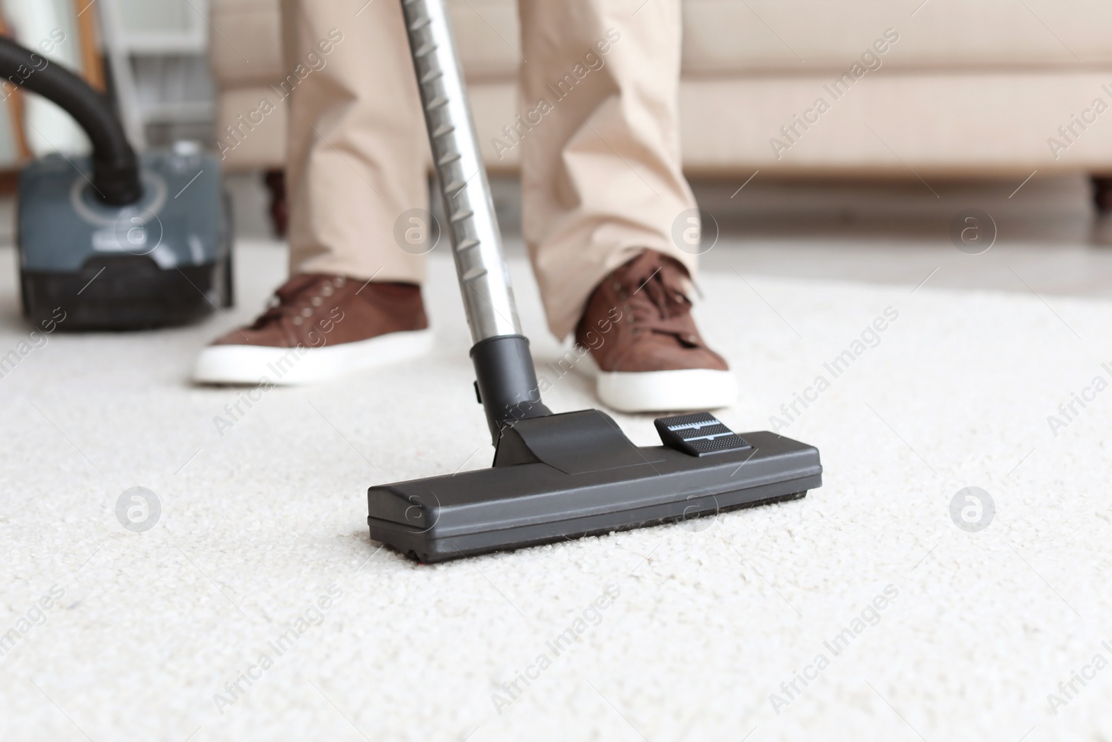 Photo of Man cleaning carpet with vacuum in living room