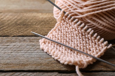 Photo of Soft beige knitting and metal needles on wooden table, closeup. Space for text