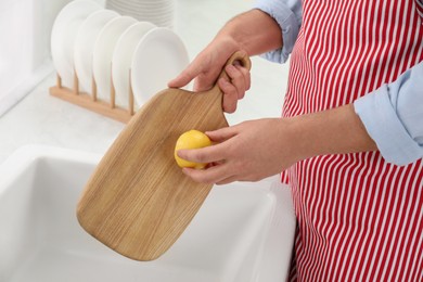 Man rubbing wooden cutting board with lemon at sink in kitchen, closeup