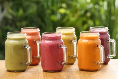 Photo of Many different delicious smoothies in mason jars on wooden table against blurred background