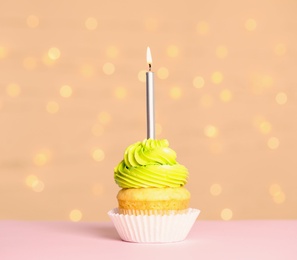 Birthday cupcake with candle on table against festive lights