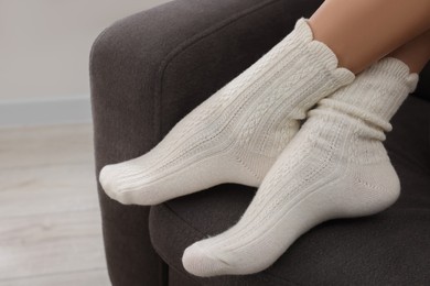 Photo of Woman in warm socks relaxing on armchair at home, closeup