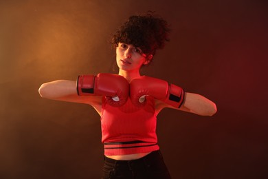 Photo of Beautiful young woman with boxing gloves on color background in neon lights