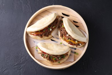 Photo of Delicious gua bao in bamboo steamer on black table, top view
