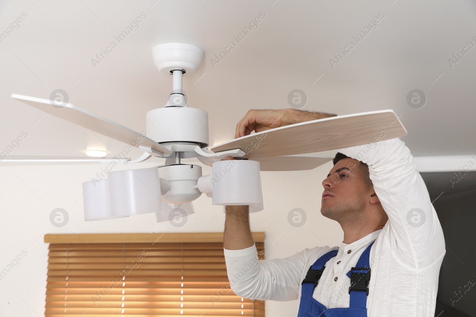 Photo of Electrician repairing ceiling fan with lamps indoors