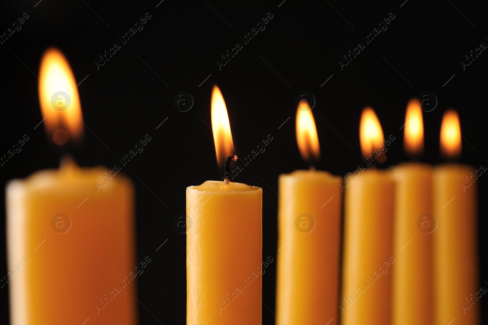 Photo of Many burning church candles on black background, closeup