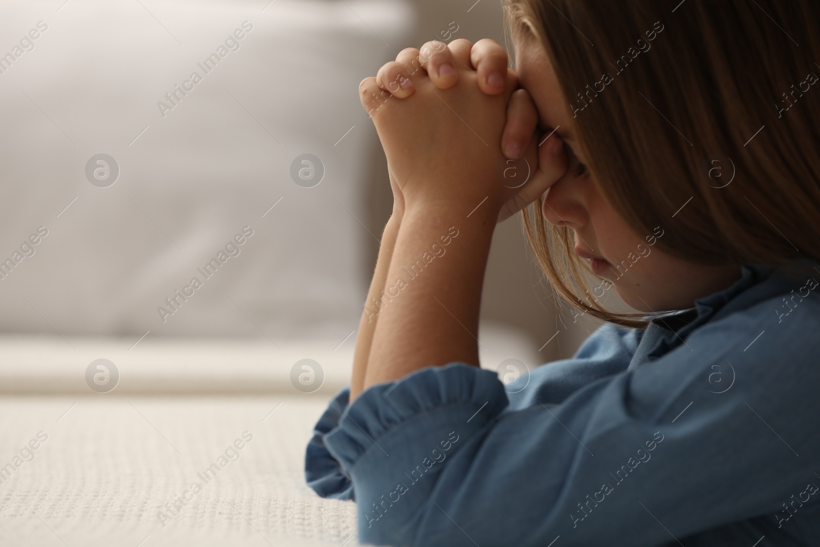 Photo of Cute little girl with hands clasped together saying bedtime prayer in bedroom. Space for text