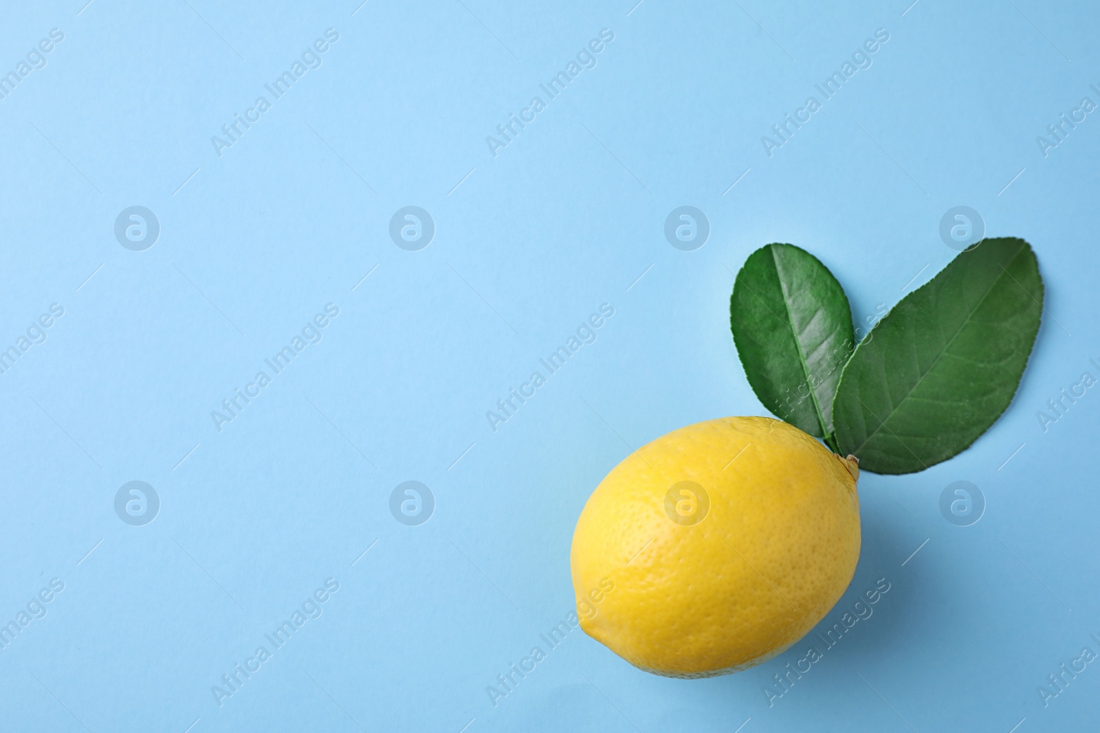 Photo of Ripe fresh lemon and leaves on light blue background, top view. Space for text