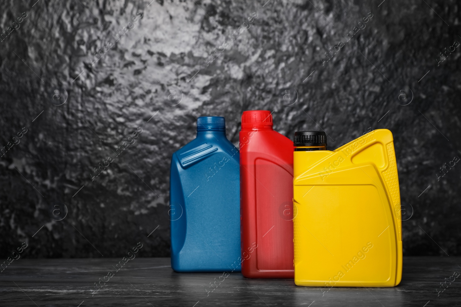 Photo of Motor oil in different canisters on black table near dark wall, space for text