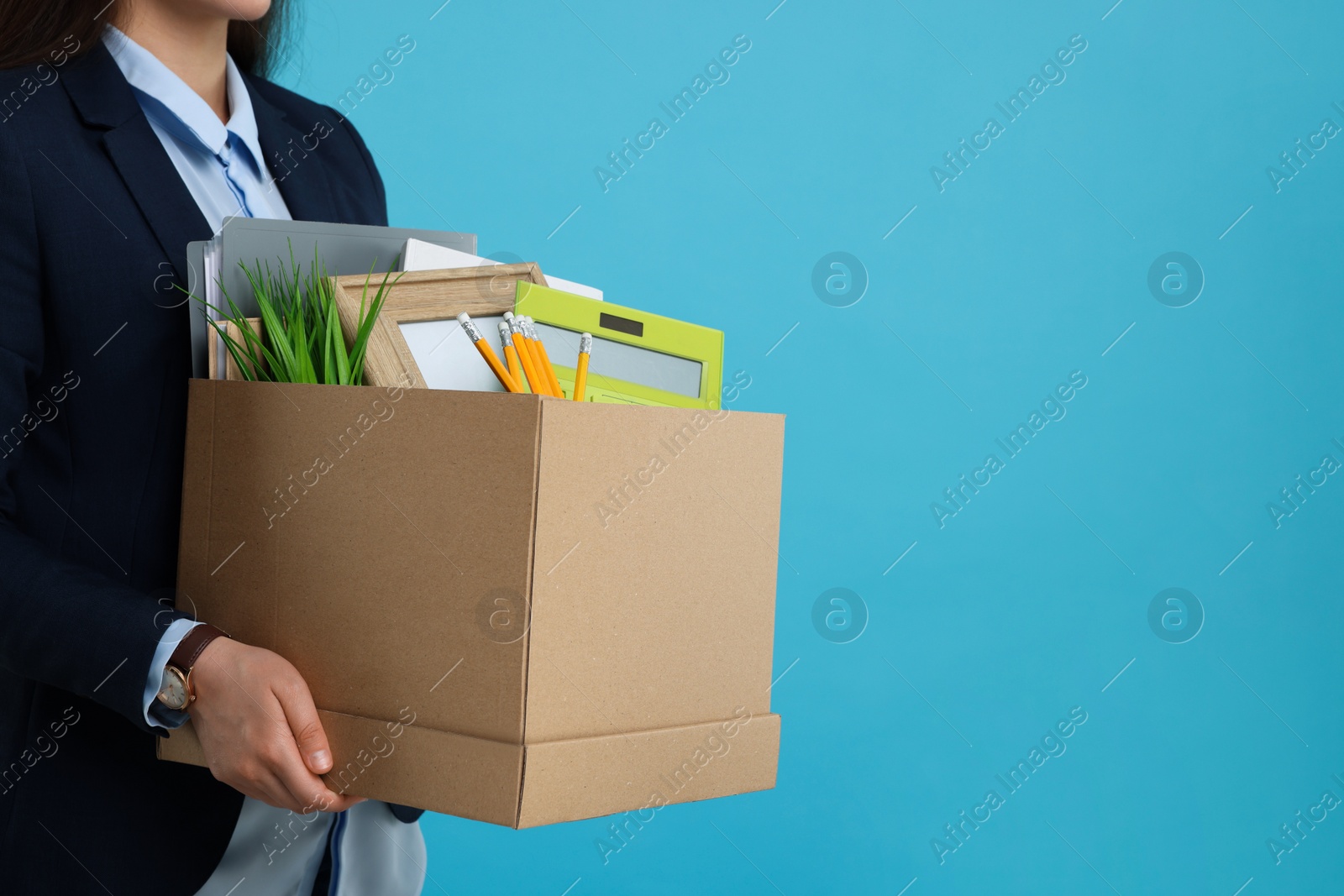 Photo of Unemployed woman with box of personal office belongings on light blue background, closeup. Space for text