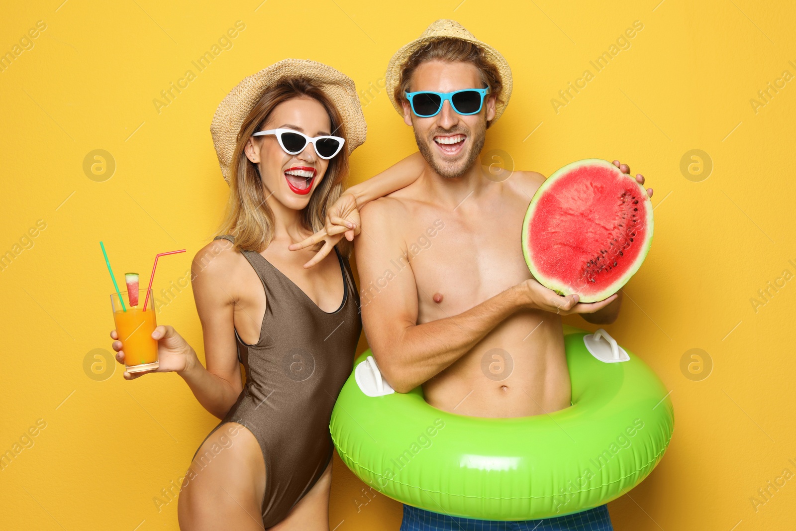 Photo of Happy young couple in beachwear with inflatable ring and cocktail on color background