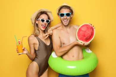 Happy young couple in beachwear with inflatable ring and cocktail on color background