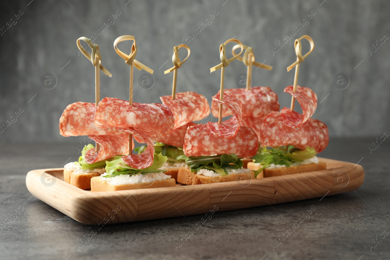 Photo of Tasty canapes with salami, greens and cream cheese on grey table