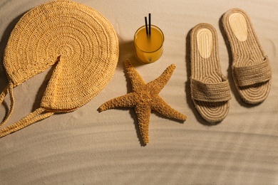 Different beach accessories and glass of cocktail on sand, flat lay