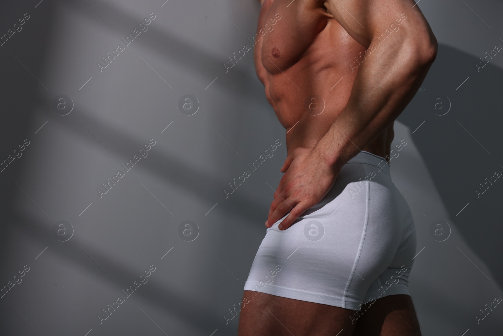 Photo of Young man in stylish white underwear near grey wall, closeup. Space for text