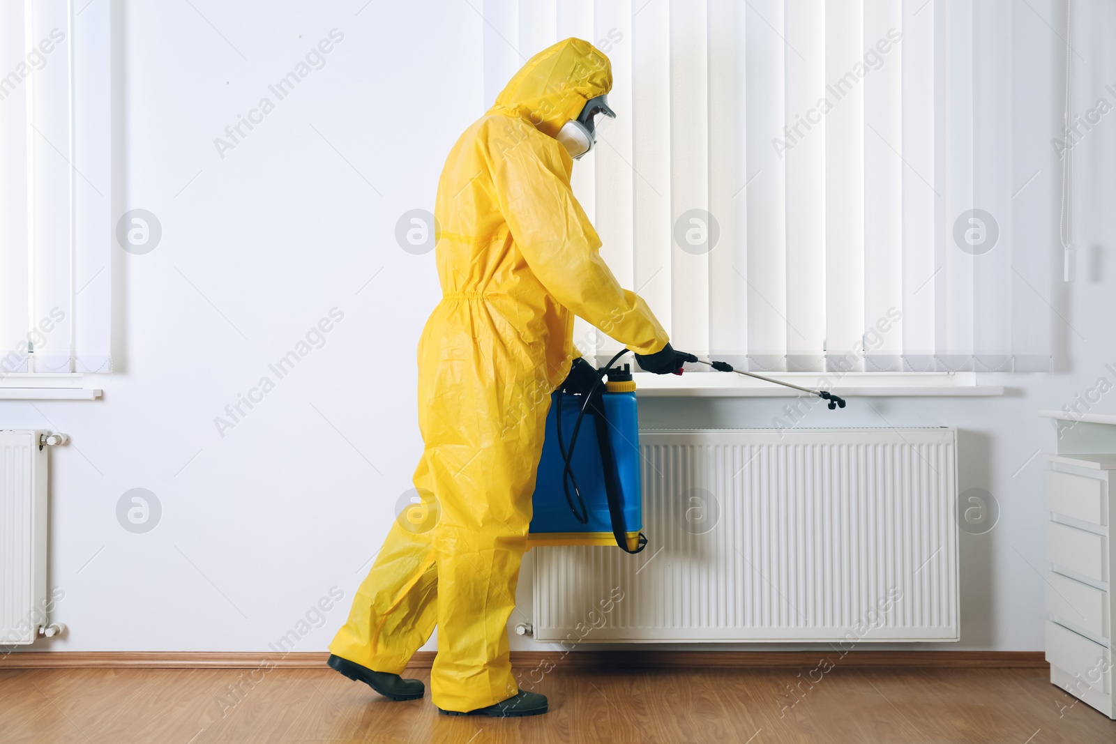 Photo of Pest control worker in protective suit spraying pesticide indoors