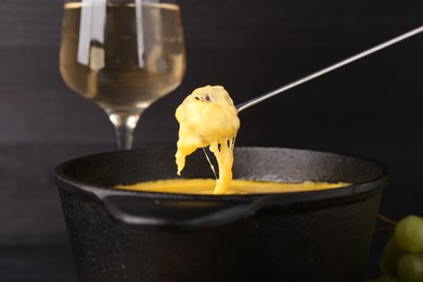 Photo of Dipping piece of bread into fondue pot with melted cheese on table, closeup