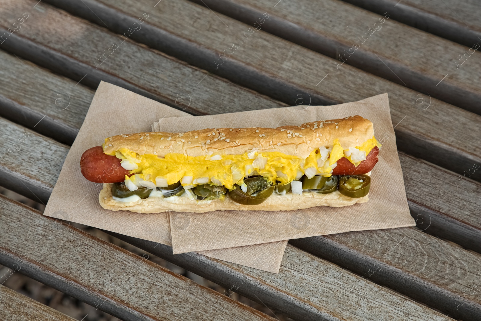 Photo of Fresh tasty hot dog with sauce on wooden surface outdoors, above view