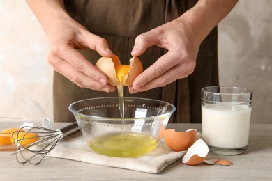 Photo of Woman separating egg yolk from white over glass bowl at light wooden table, closeup