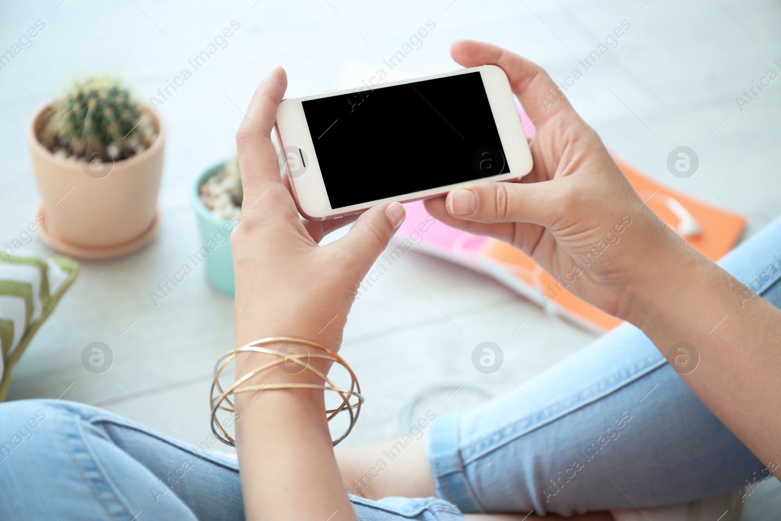 Photo of Young woman holding mobile phone with blank screen in hands, indoors