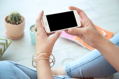 Photo of Young woman holding mobile phone with blank screen in hands, indoors