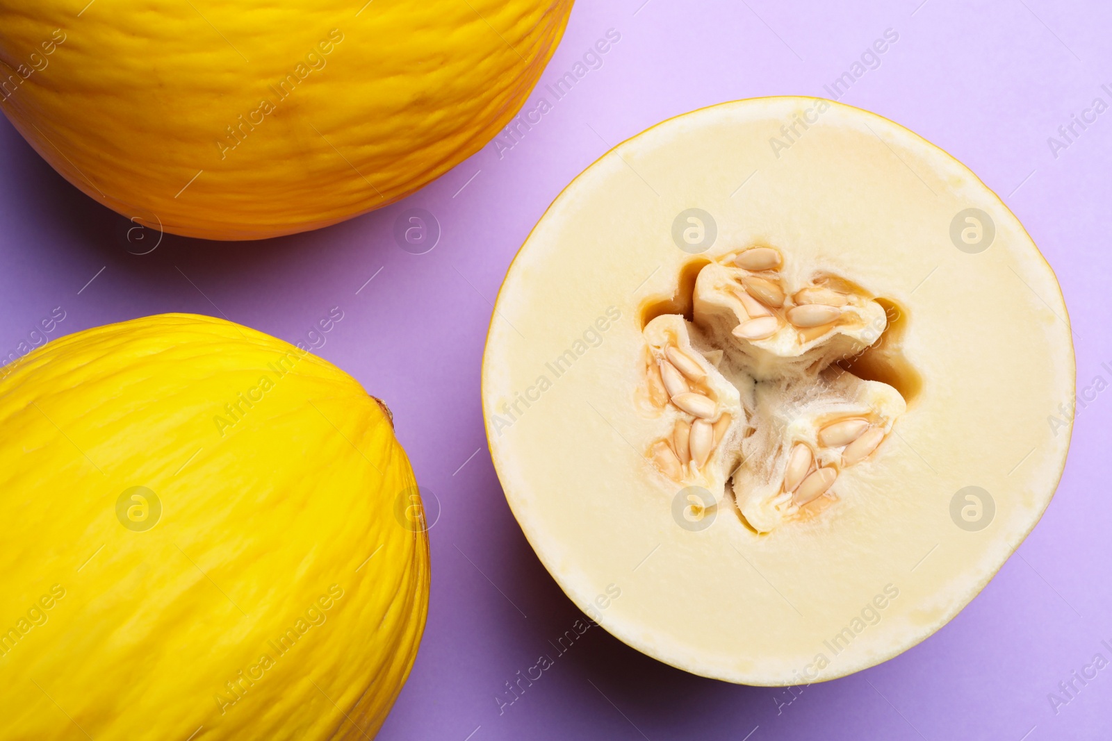 Photo of Ripe tasty melons on violet background, flat lay