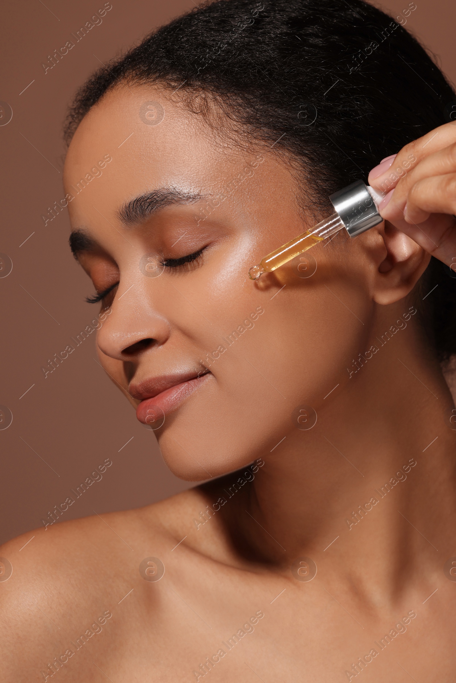 Photo of Beautiful woman applying serum onto her face on brown background