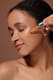 Beautiful woman applying serum onto her face on brown background