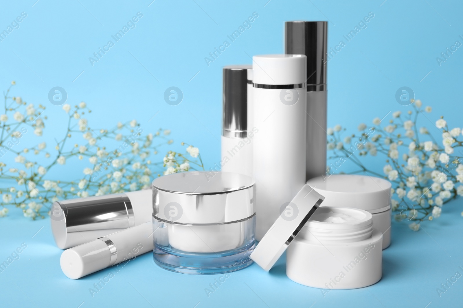 Photo of Set of luxury cosmetic products and flowers on light blue background
