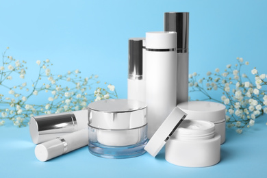 Photo of Set of luxury cosmetic products and flowers on light blue background