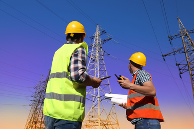 Professional electricians in uniforms near high voltage towers