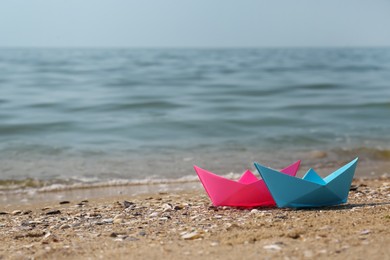 Bright paper boats on sandy beach near sea, space for text