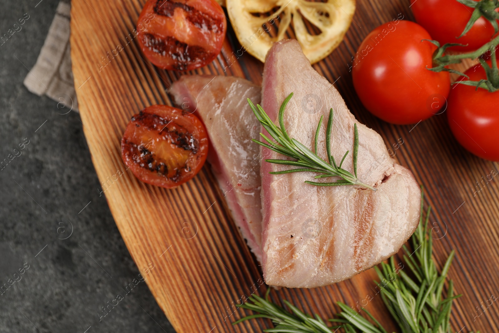Photo of Pieces of delicious tuna steak with rosemary, tomatoes and lemon on grey table, top view