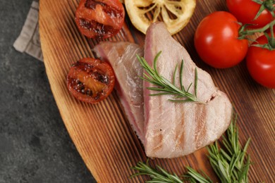 Photo of Pieces of delicious tuna steak with rosemary, tomatoes and lemon on grey table, top view