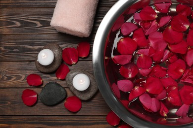 Photo of Bowl with water, red rose petals, stones and burning candles on wooden floor, flat lay. Pedicure procedure