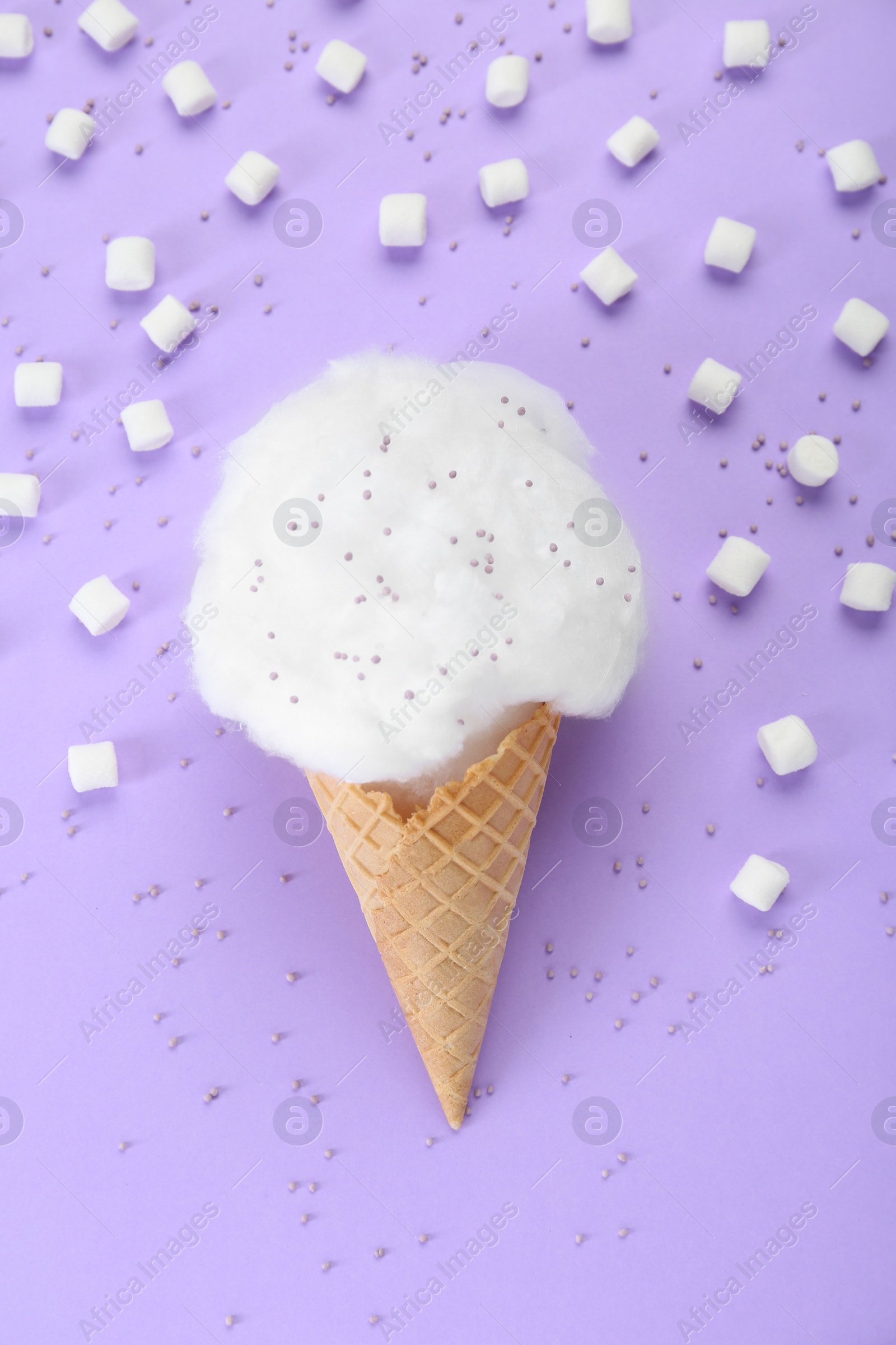 Photo of Sweet cotton candy in waffle cone and marshmallows on purple background, flat lay