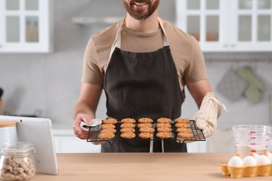 Photo of Man holding grid with freshly baked cookies in kitchen, closeup. Online cooking course