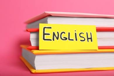 Sheet of paper with word English and books on pink background, closeup
