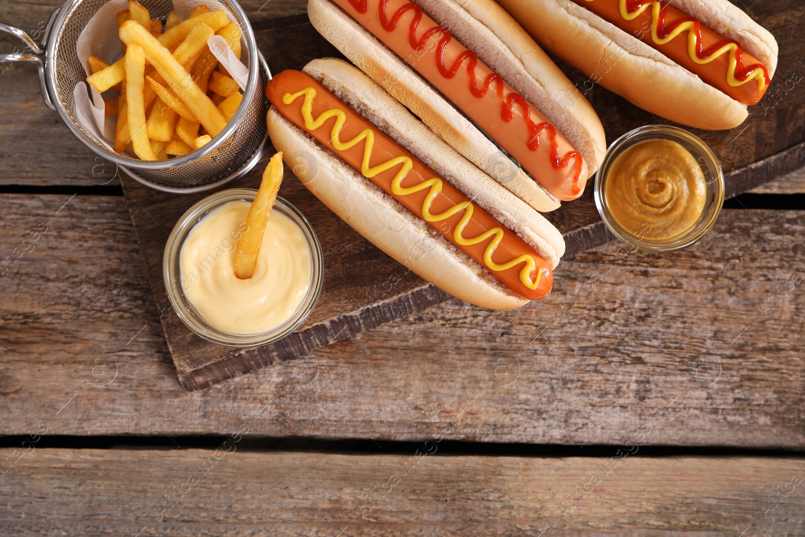 Photo of Delicious hot dogs with sauces and French fries on wooden table, top view. Space for text