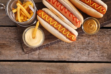 Delicious hot dogs with sauces and French fries on wooden table, top view. Space for text