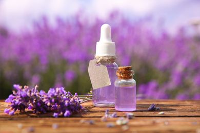 Photo of Bottles of natural essential oil and lavender flowers on wooden table
