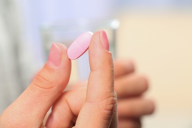 Woman holding pill and glass of water on blurred background, closeup. Space for text